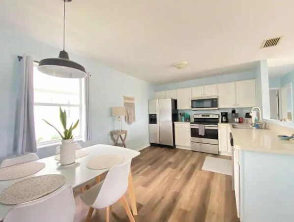 A modern kitchen with white cabinets, stainless steel appliances, and a wooden floor.