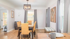 Comedor con mesa de madera y sillas de mimbre, lámpara colgante y un banco con cojín a rayas.