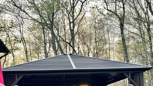 Een overdekt terras met een tuinhuisje, een bank en een hottub.