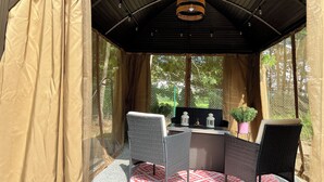 Een overdekt terras met een tafel en stoelen, een hanglamp en uitzicht op groen door het raam.