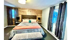 Een slaapkamer met een groot bed, twee nachtkastjes, een hoofdeinde en een raam met gordijnen.