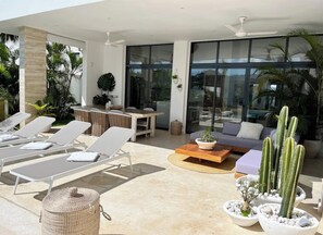 Relax in a serene space with a seating area, lounge chairs, and a table, surrounded by lush greenery and a large window offering a view of the outdoors.