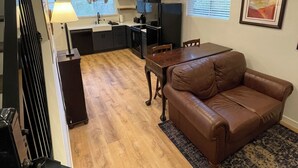 A modern kitchen with a central island, a dining area with a brown leather sofa, and a staircase leading to an upper level. - Adorable Brand New Studio Barn Loft with Full Kitchen and Bath (Provo)