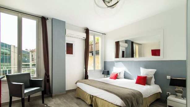 Une chambre d’hôtel avec un lit, une chaise, une table de chevet et une fenêtre avec des rideaux.