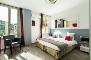 A hotel room with a bed, a chair, a bedside table, and a window with curtains. - Florella Residences Studio République (Cannes)