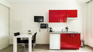 Une cuisine de taille réduite avec une table blanche, des placards rouges, un four à micro-ondes et un petit réfrigérateur.
