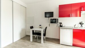 Une cuisine compacte avec une table blanche, des placards rouges, un four à micro-ondes et un petit lave-vaisselle.