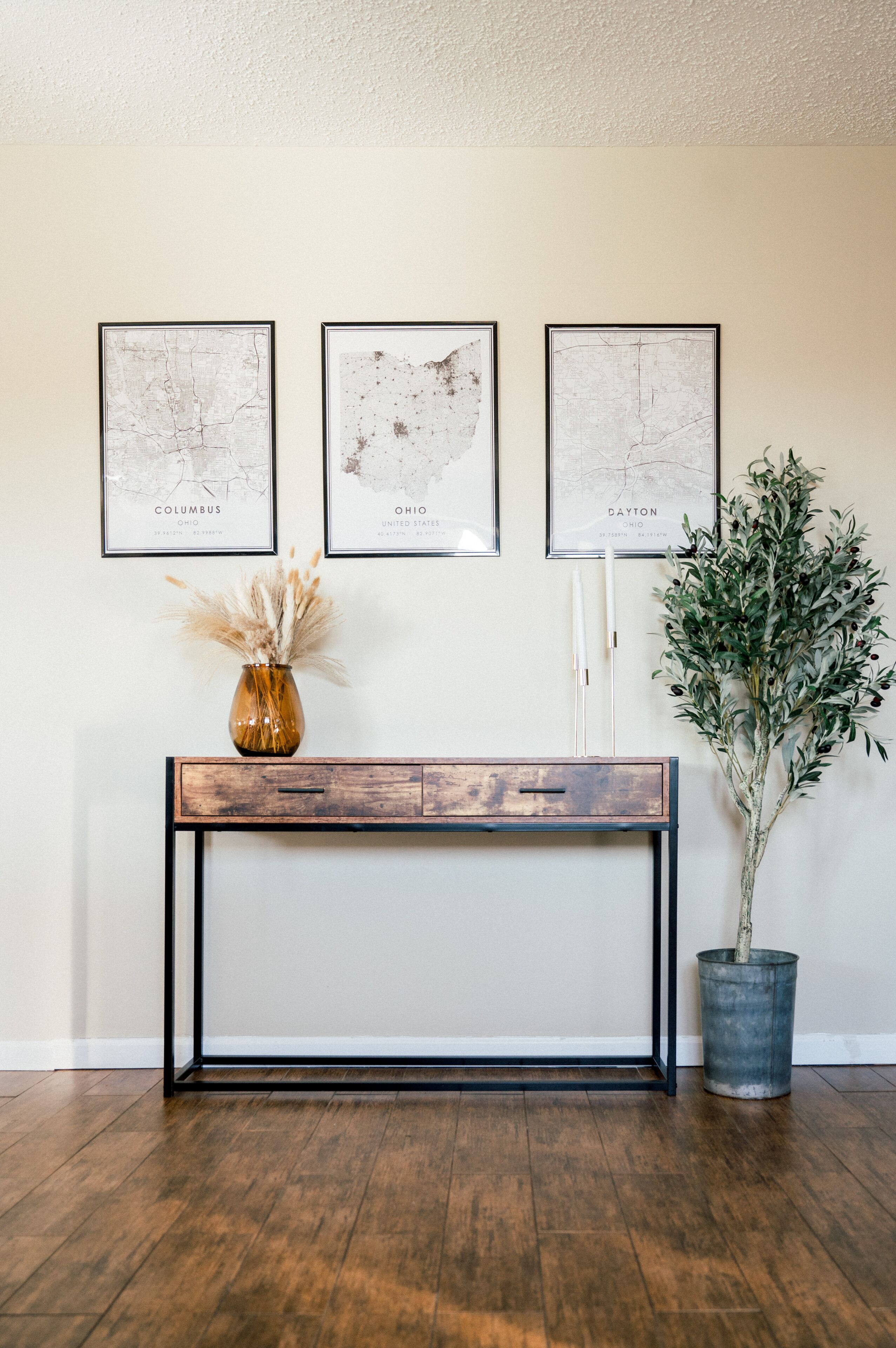 Une console en bois ornée d’un vase et de bougies, et encadrée de deux cartes de la ville de Columbus, dans l’Ohio, et de Dayton, dans l’Ohio.