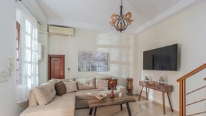 A living room with a sectional sofa, a wooden coffee table, a chandelier, a flat-screen TV, and a staircase.