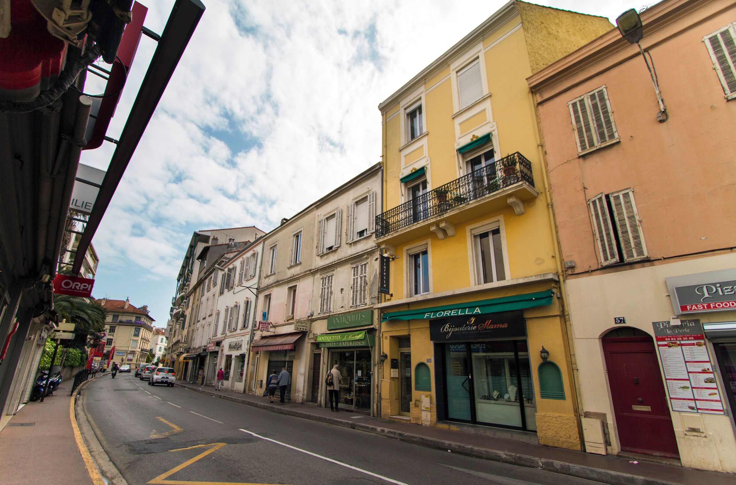 Uma rua com edifícios, incluindo um restaurante chamado "Florella" e uma lanchonete.