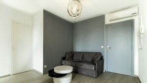 A room with a grey couch, a white and black round table, and a ceiling light fixture. - Florella Residences 2 pièces supérieur République (Cannes)