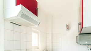 A kitchen with white and red cabinets, a stainless steel sink, and a compact refrigerator. - Florella Residences 2 pièces supérieur République (Cannes)