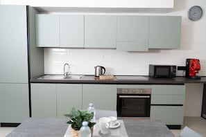 A modern kitchen with light green cabinets, a stainless steel sink, a kettle, a microwave, and a red coffee machine.