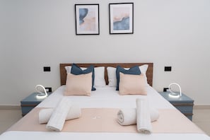 A neatly made bed with pillows, a bedside table with a lamp, and two framed artworks on the wall.