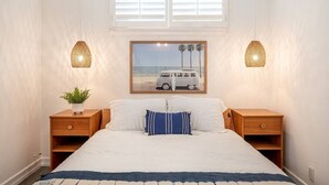 A bedroom with a bed, two nightstands, a potted plant, a framed picture, and a window with blinds.