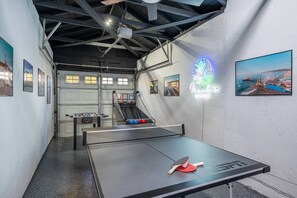 Een tafeltennistafel in een ruimte met een neonbord, een tafelvoetbaltafel en uitzicht op een kustgebied.