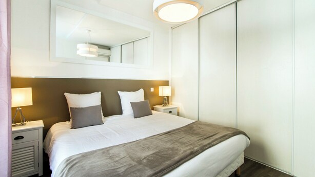 Una habitación de hotel moderna con una cama grande, lámparas de noche, un espejo y un armario.