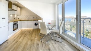 A modern kitchen with a built-in washing machine, a dining area with a glass table, and large windows offering a city view. - The Penthouse, Beautiful sea views, Centre of Oban (Oban)