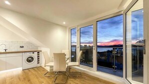 A modern kitchen with a washing machine, a dining area with a chair, and large windows with a city view. - The Penthouse, Beautiful sea views, Centre of Oban (Oban)