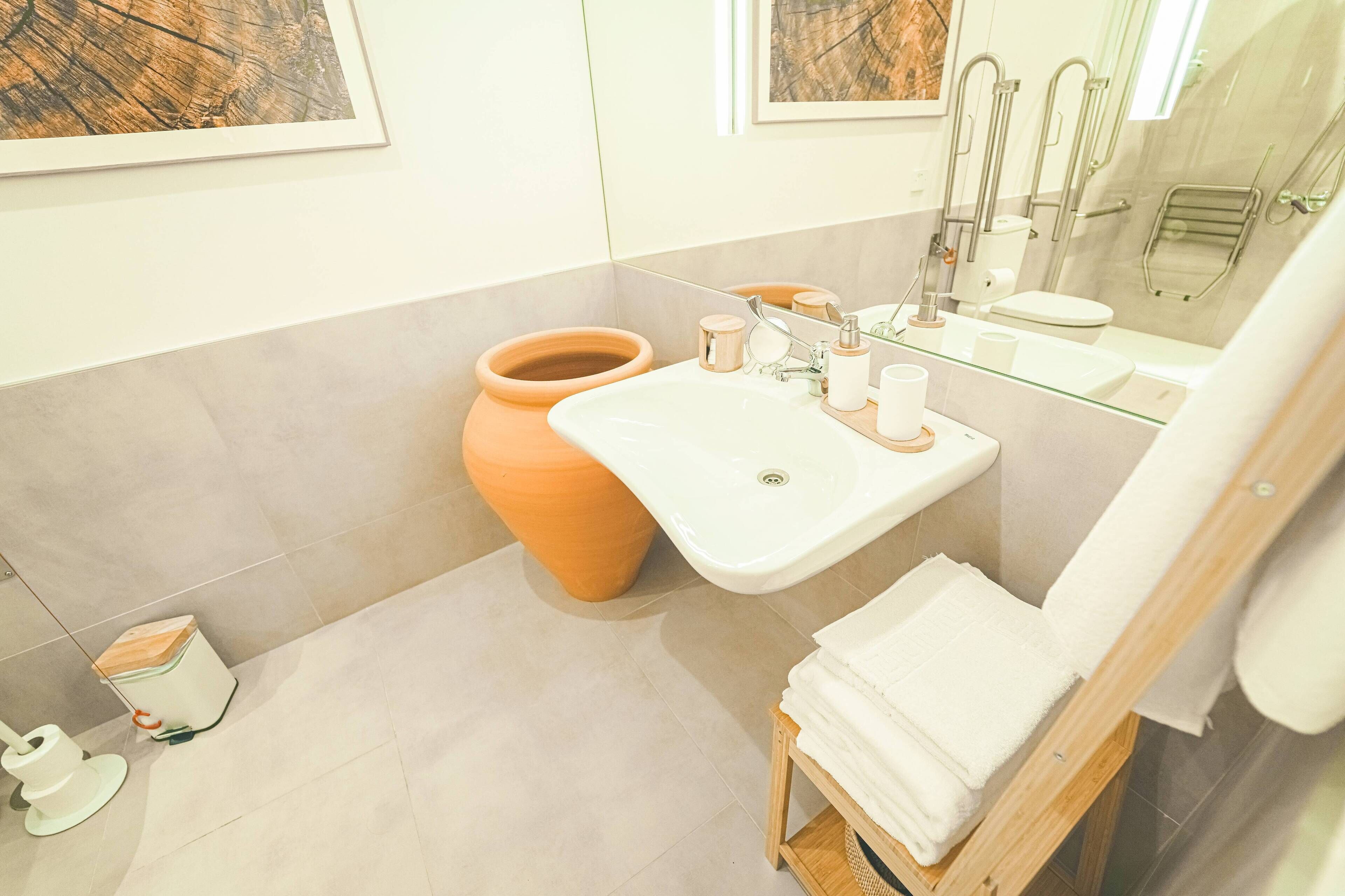 A modern bathroom with a white sink, a mirror, a toilet, and a shower area.