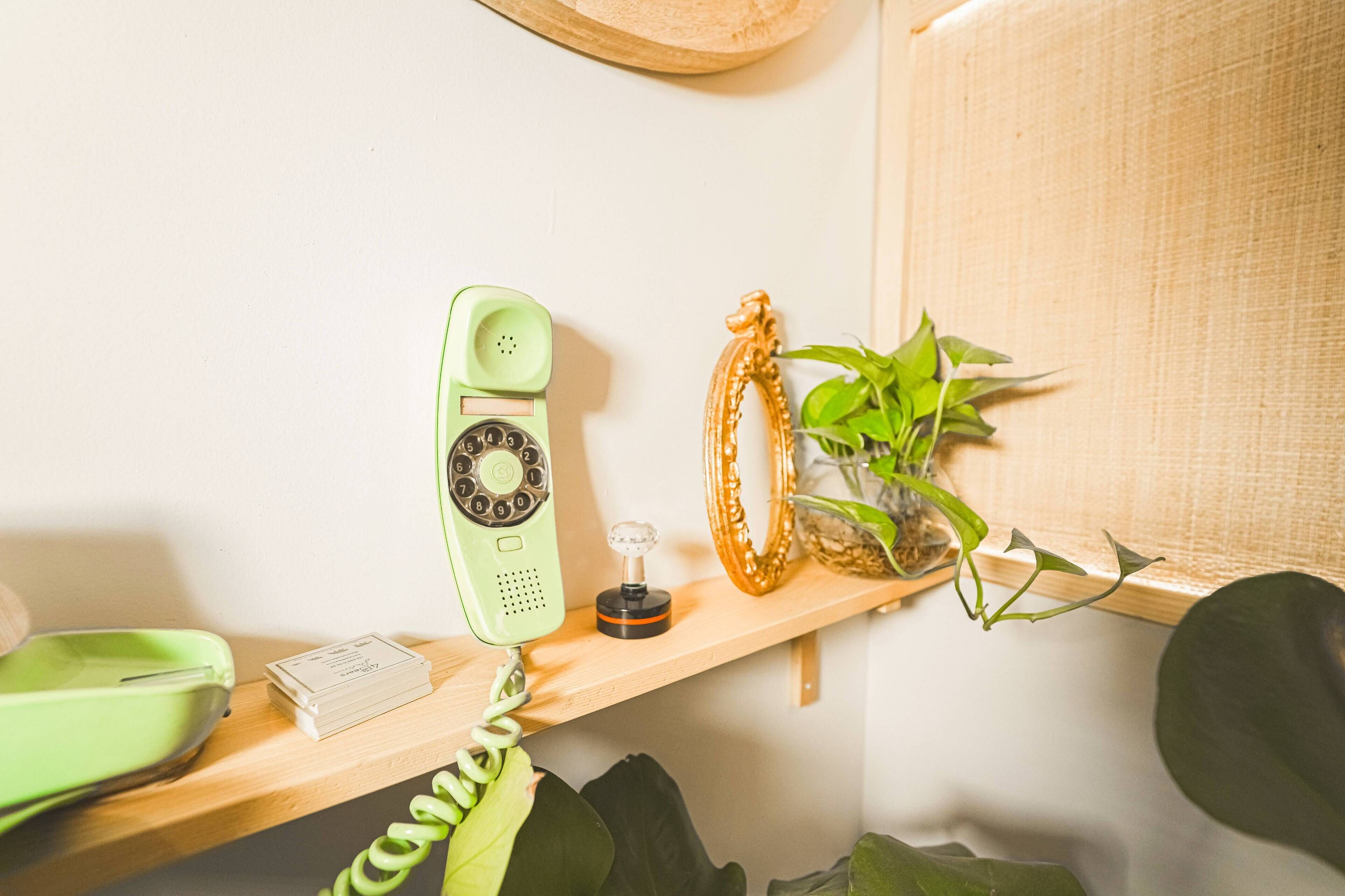 A green rotary phone on a wooden shelf, a small plant, and a decorative item.