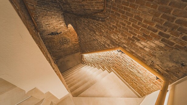 Una scala con un muro in mattoni da un lato e un muro bianco dall'altro, che conduce a un livello inferiore.