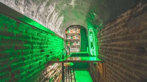 Un tunnel stretto con pareti in mattoni, che ospita un'area bar con sgabelli e scaffali pieni di bottiglie.