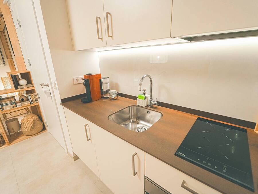 Eine moderne Küche mit Spüle aus Edelstahl, schwarzem Induktionskochfeld und weißen Schränken.