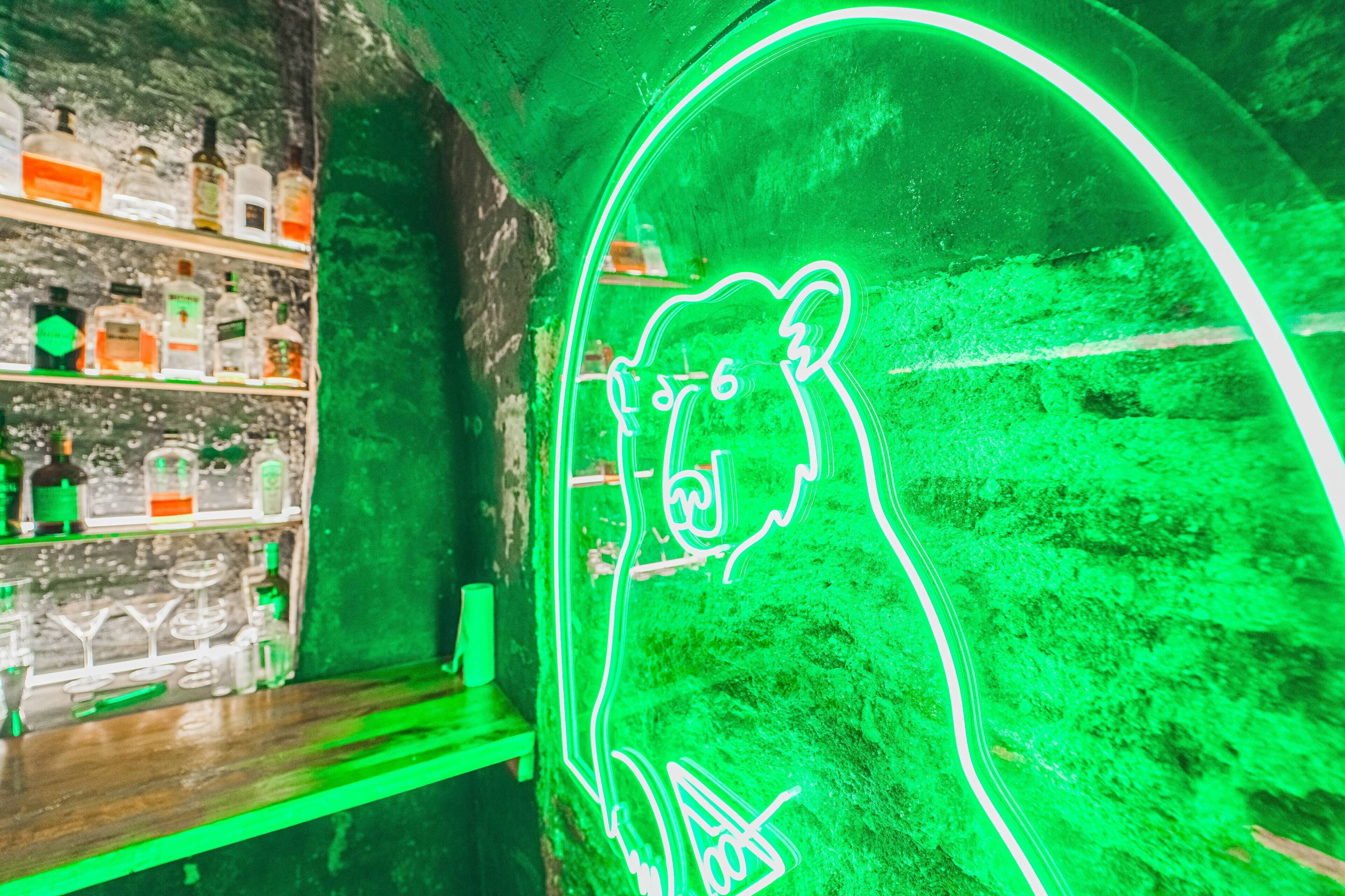 A neon sign with a bear design, a shelf with liquor bottles, and a rustic wall.