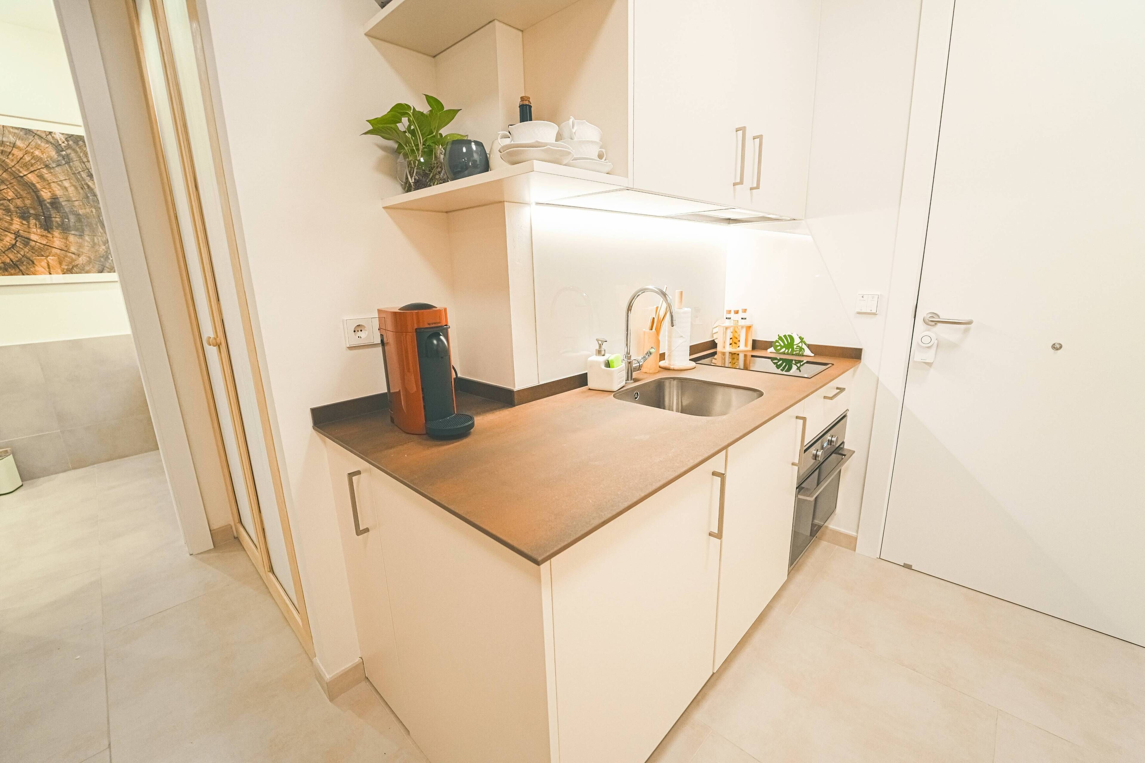 Una cocina moderna con encimera de madera, armarios blancos, horno empotrado y un lavabo.
