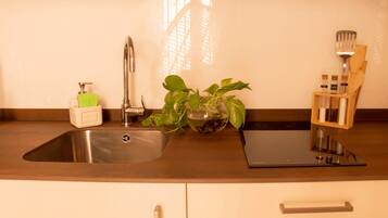 A kitchen with a stainless steel sink, a faucet, a plant, and a wooden utensil holder.