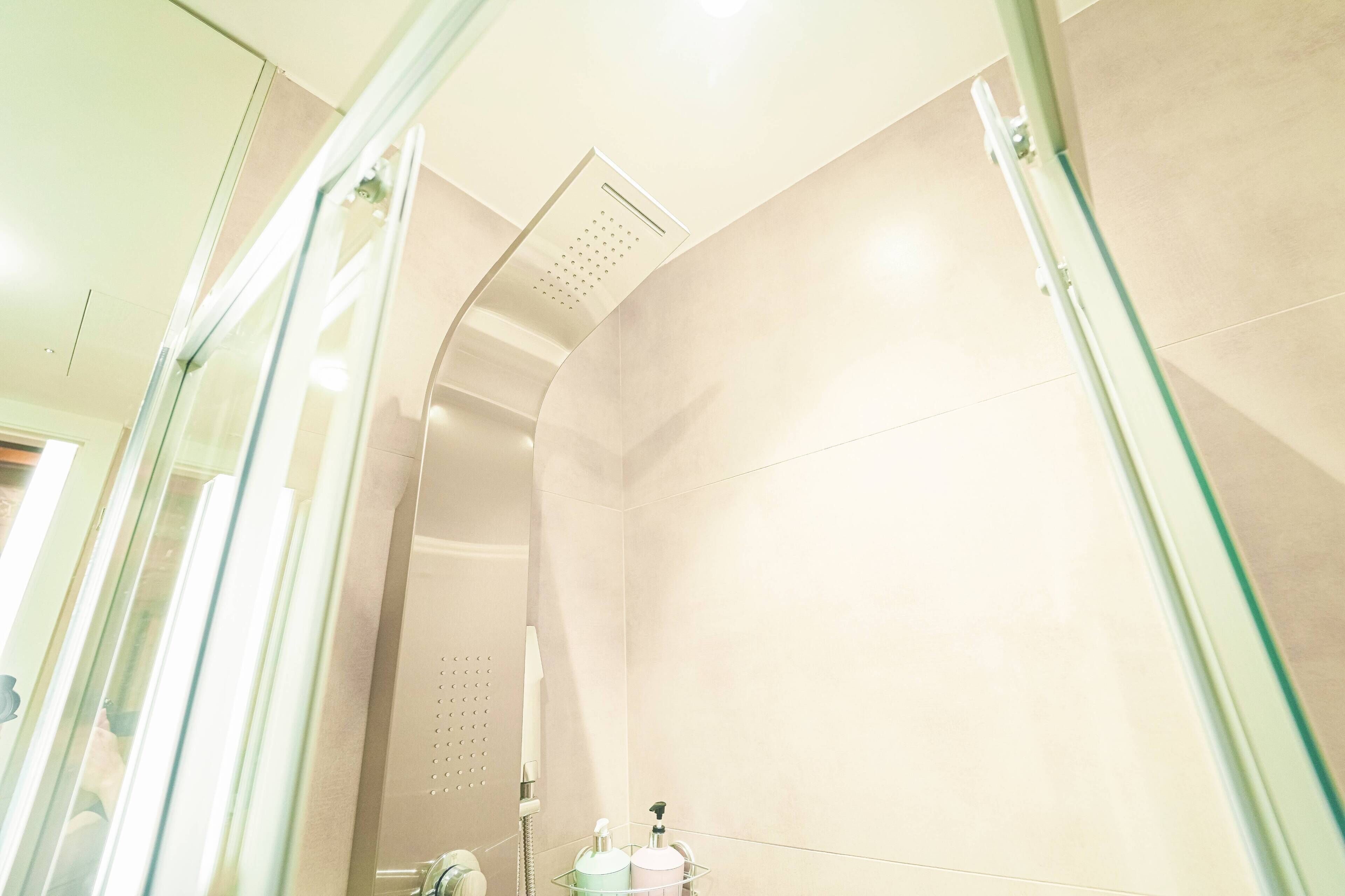 Un baño moderno con cabina de ducha de vidrio, un cabezal de ducha manual y un dispensador de jabón en el lavamanos.