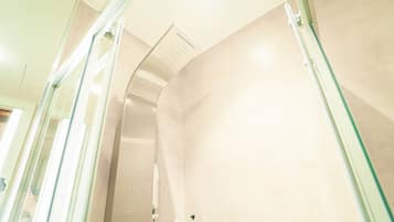 Un baño moderno con cabina de ducha de vidrio, un cabezal de ducha manual y un dispensador de jabón en el lavamanos.