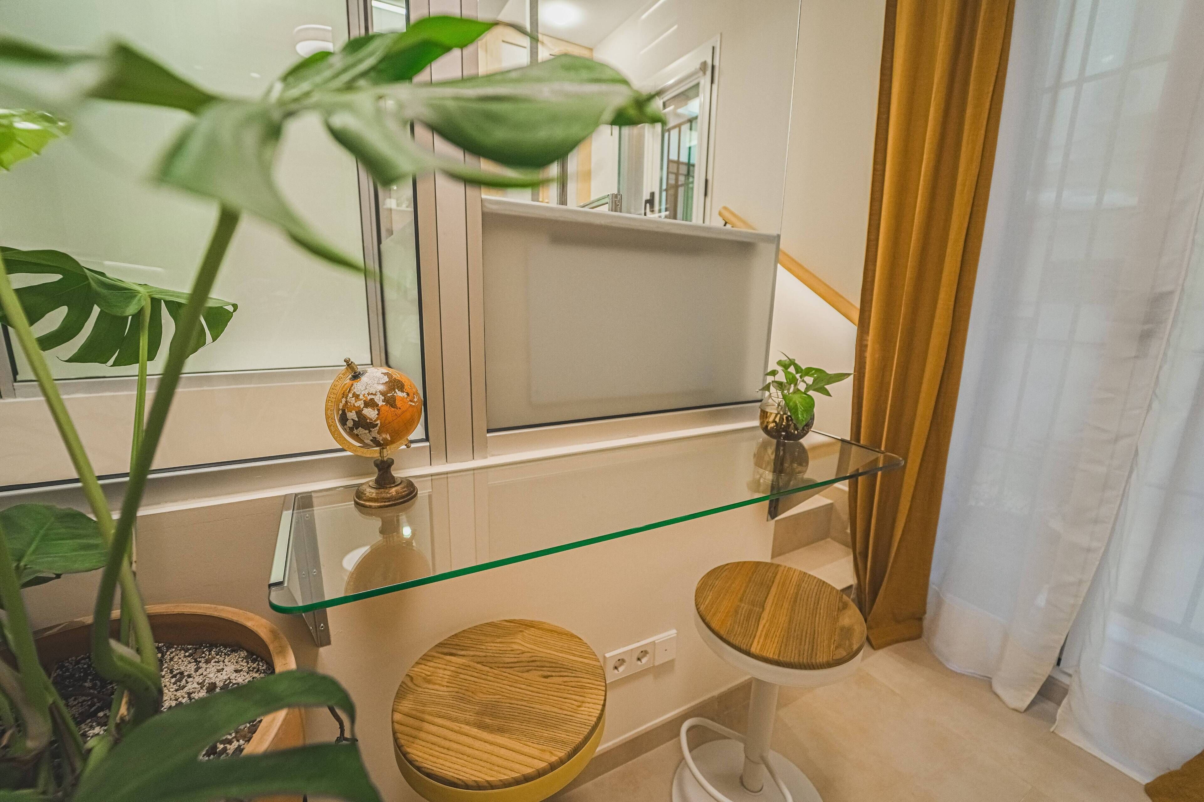 Ein modernes Badezimmer mit einer Glasablage, Holzschemeln, einem Blumentopf und einem Spiegel.