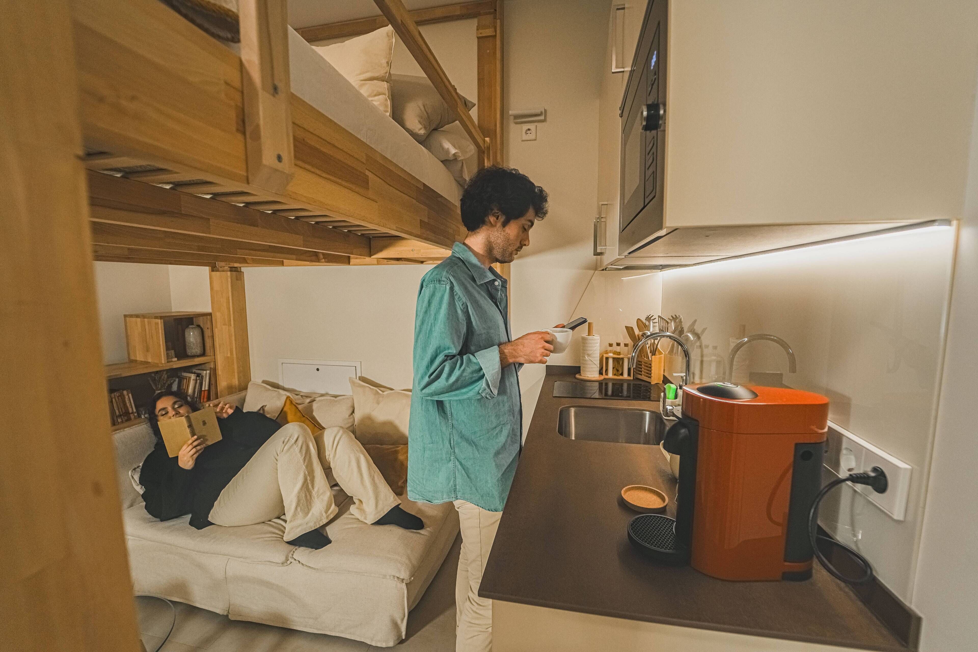 A compact kitchen with a built-in oven, a sink, and a compact orange appliance, likely a vacuum cleaner.