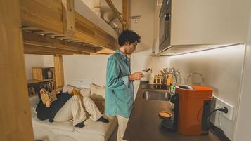 A compact kitchen with a built-in oven, a sink, and a compact orange appliance, likely a vacuum cleaner.