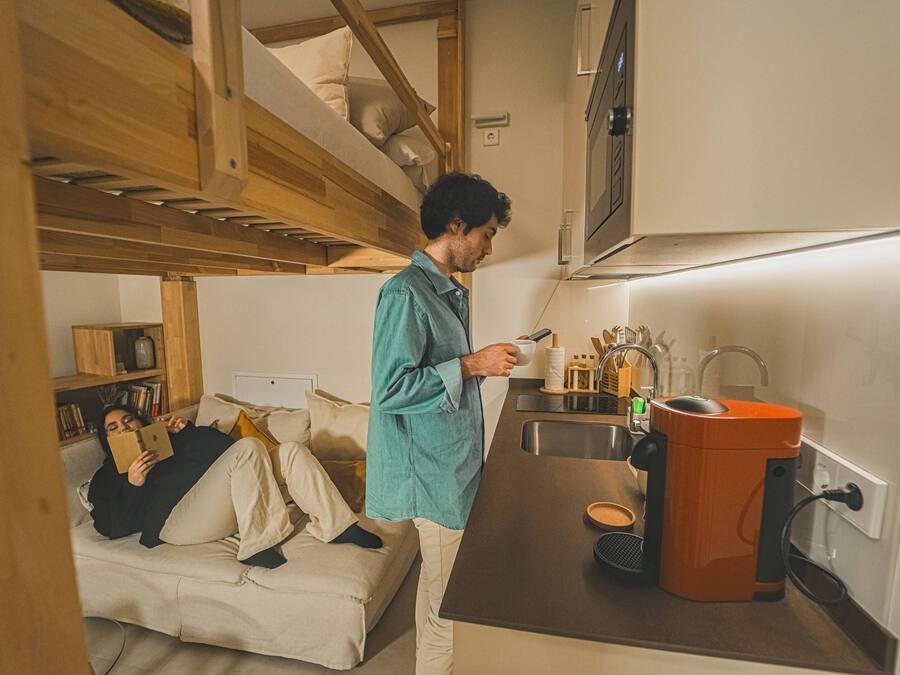 A compact kitchen with a built-in oven, a sink, and a compact orange appliance, likely a vacuum cleaner.