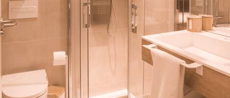 Un baño moderno con cabina de ducha de vidrio, inodoro y lavamanos con espejo.