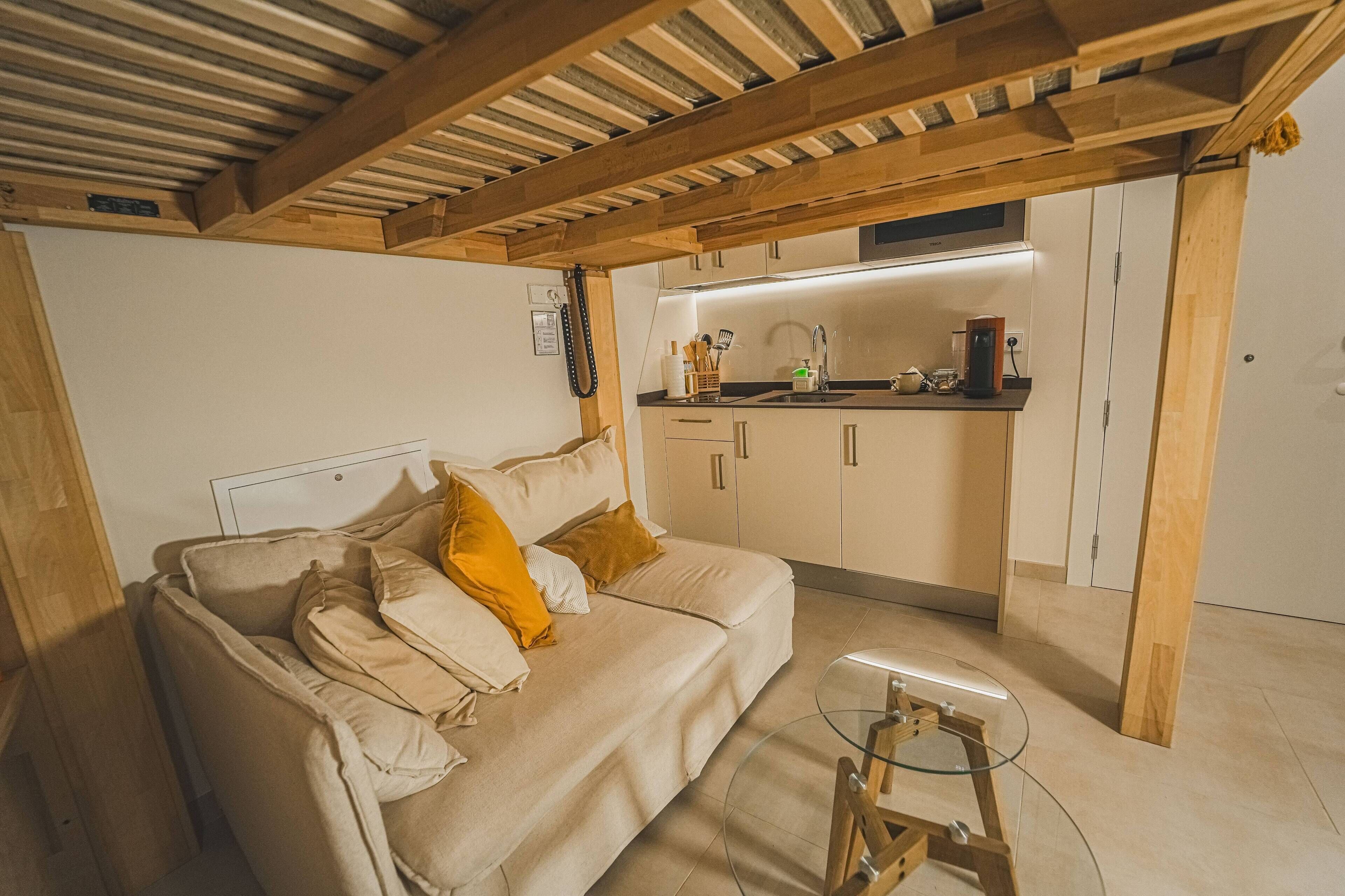 Una sala de estar acogedora con un sofá, una mesa de centro de vidrio y una cocina con armarios y encimera.