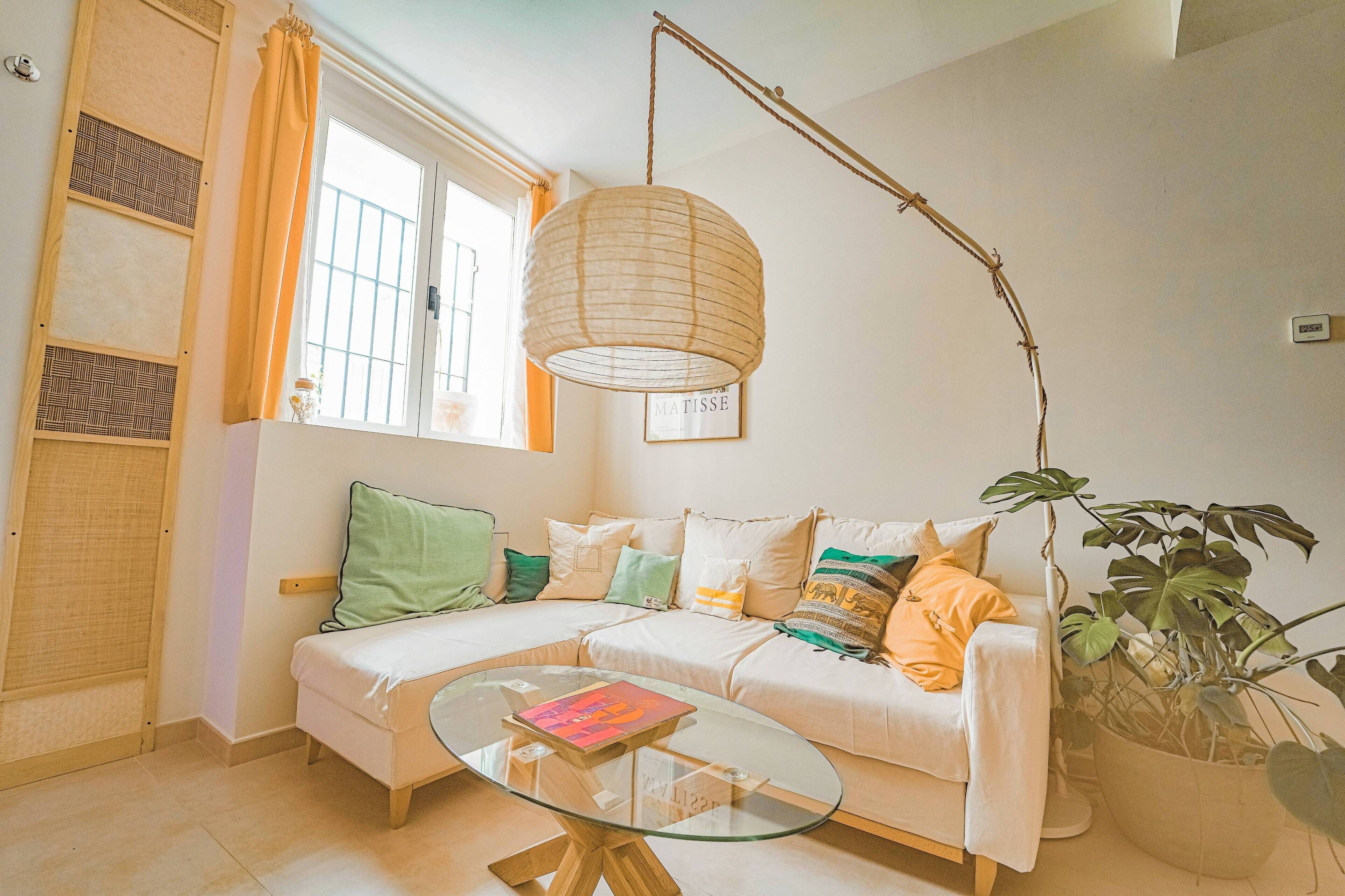 A cozy living room with a white sofa, a glass coffee table, and a hanging light fixture.