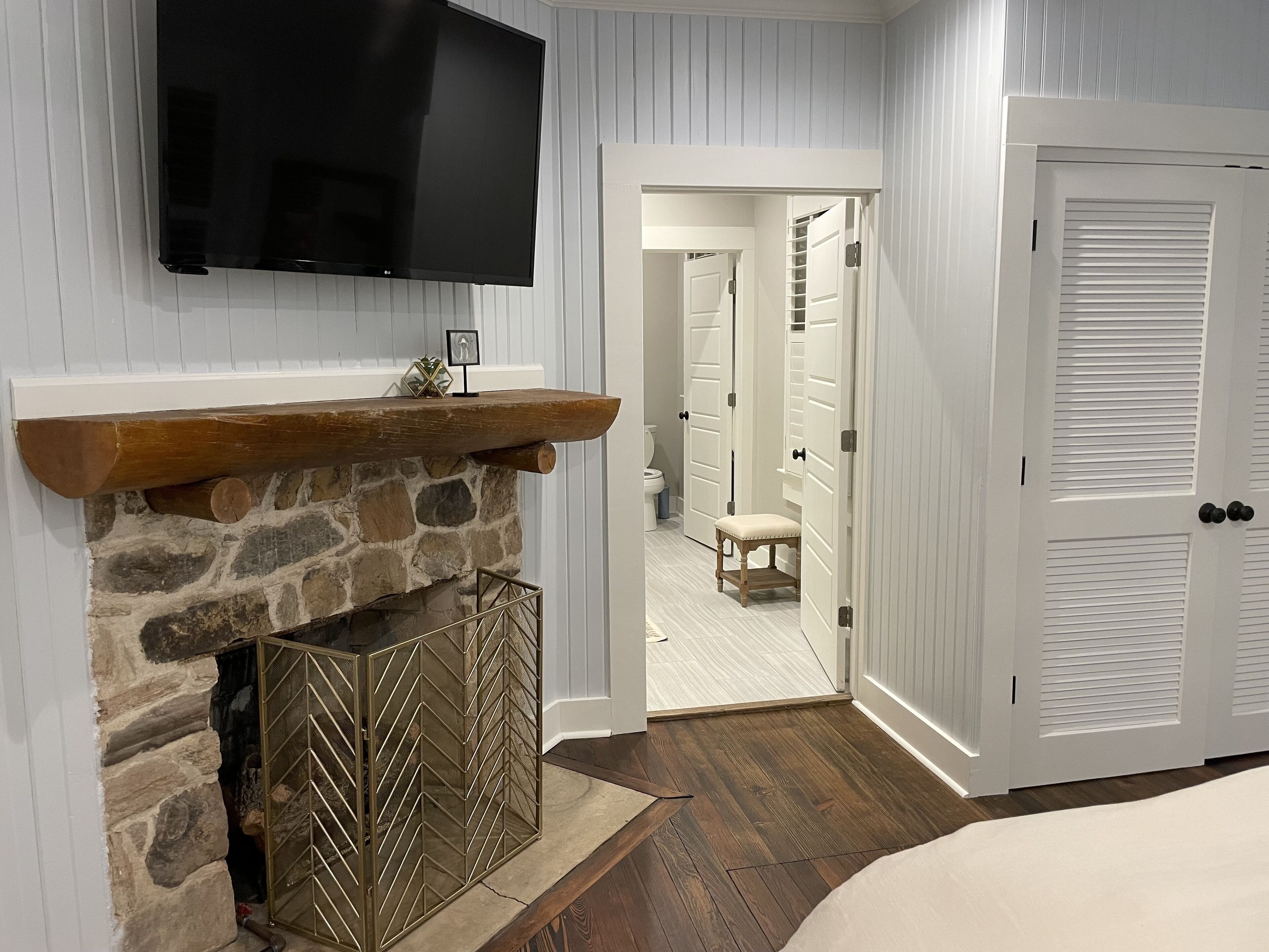 Une chambre avec une cheminée en pierre, un téléviseur fixé au mur et un banc en bois.