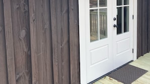 Una puerta principal blanca con paneles de vidrio, revestimiento de madera oscura y una pequeña lámpara arriba.
