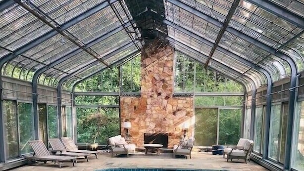 Un área de piscina con chimenea de piedra, sillones de descanso y techo de cristal.