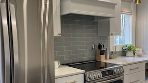 Una cocina moderna con electrodomésticos de acero inoxidable, armarios blancos y salpicadero de azulejos grises.