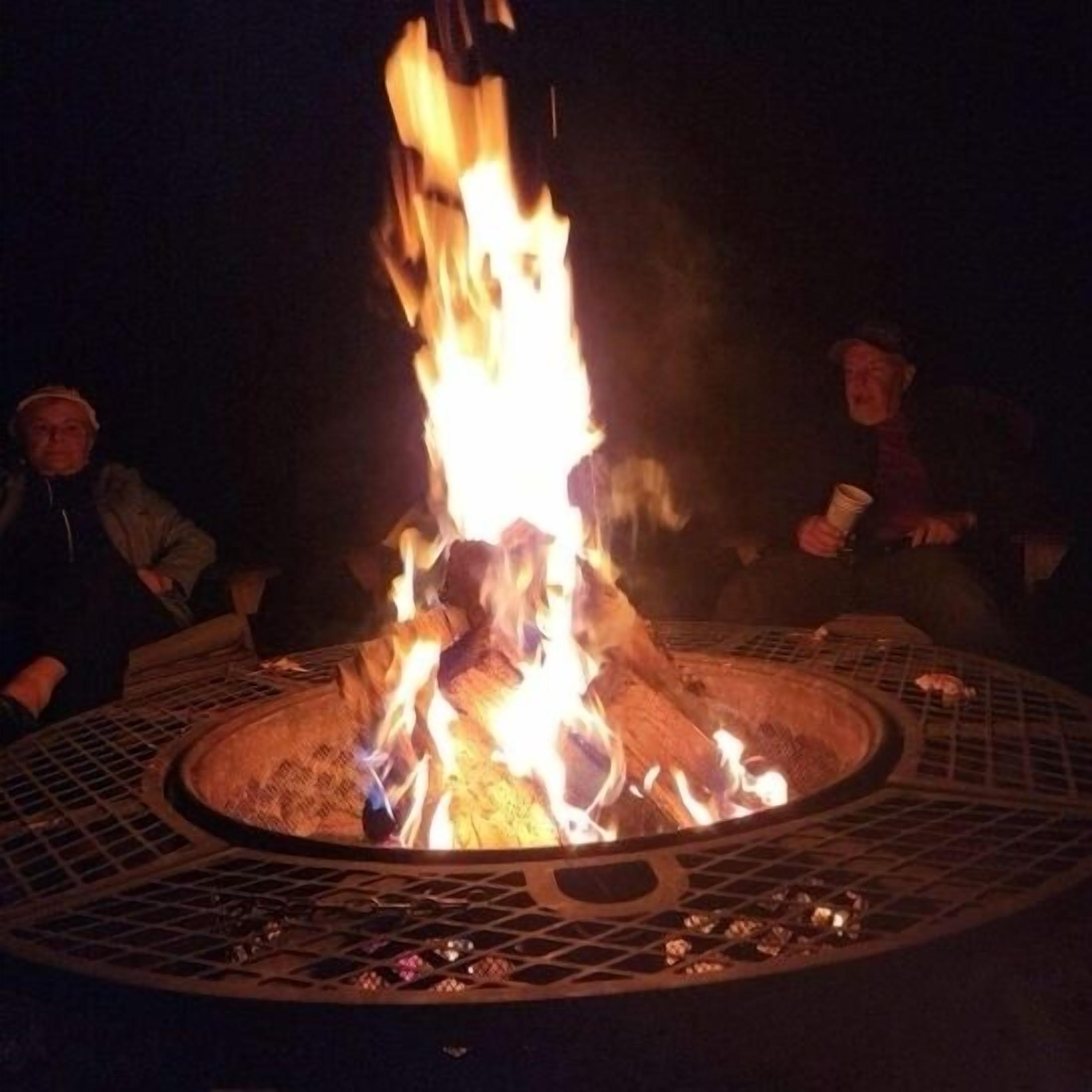 A circular outdoor fire pit with flames, surrounded by a metal grill.