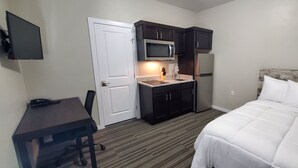 Een hotelkamer met een bed, een bureau met stoel, een magnetron, een koelkast en een klein kitchenette.