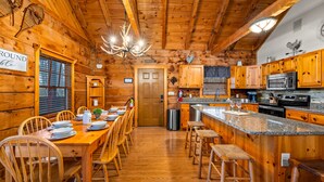 Interior de una cabaña de troncos con comedor, cocina y barra.