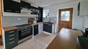 A modern kitchen with black cabinets, a stove, a dishwasher, and a wooden countertop. - Gîte des Tannières ideal for a successful stay (Pouques-Lormes)