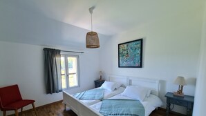 A bedroom with a bed, a chair, a nightstand, a lamp, a window with curtains, and a painting on the wall. - Gîte des Tannières ideal for a successful stay (Pouques-Lormes)