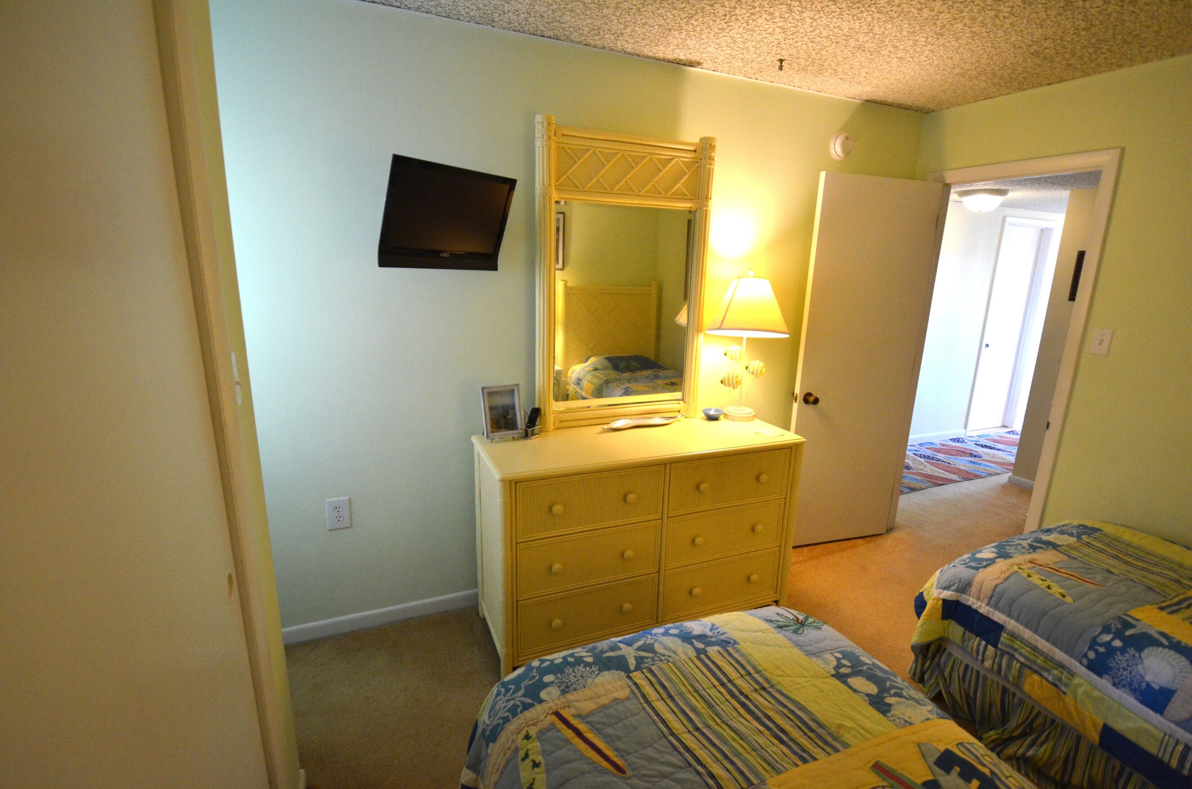 Une chambre à coucher comprenant un lit, une commode, un miroir, un téléviseur et une porte donnant sur une autre pièce.